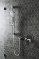 Brausekombination von Ideal Standard mit einem Chrom-Haltegriff und einem Handbrausekopf, montiert an einer Wand mit sechseckigem Fliesenmuster.